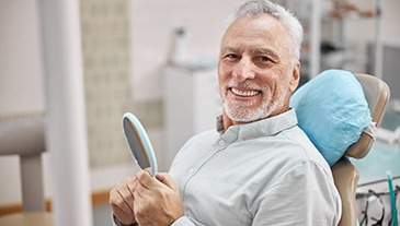 patient smiling while holding dental mirror 