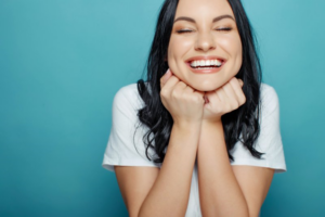 Woman smiling wide with eyes closed on blue background