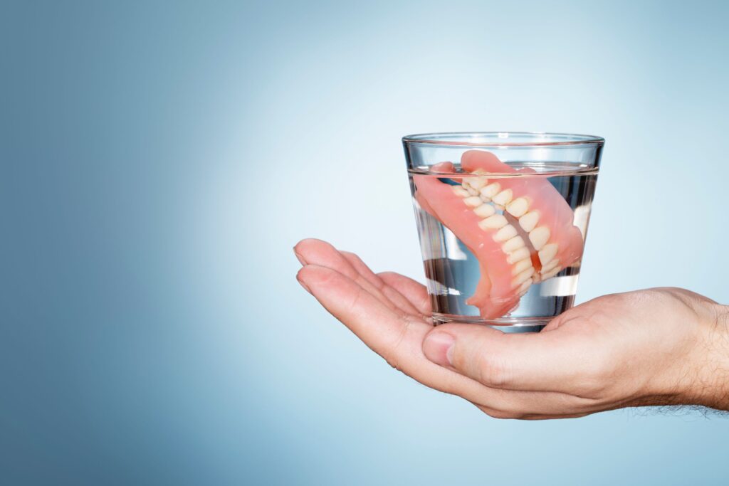 Dentures in a glass of clear fluid held in the palm of a hand